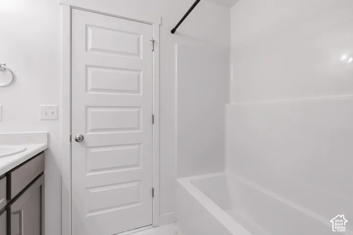 White paneled door, gray vanity cabinetry, light countertop, integral sink, and white shower/tub combination