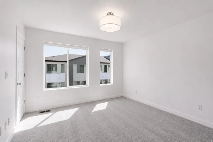 Two large windows, flush-mounted ceiling light fixture, neutral wall paint, and gray carpet flooring