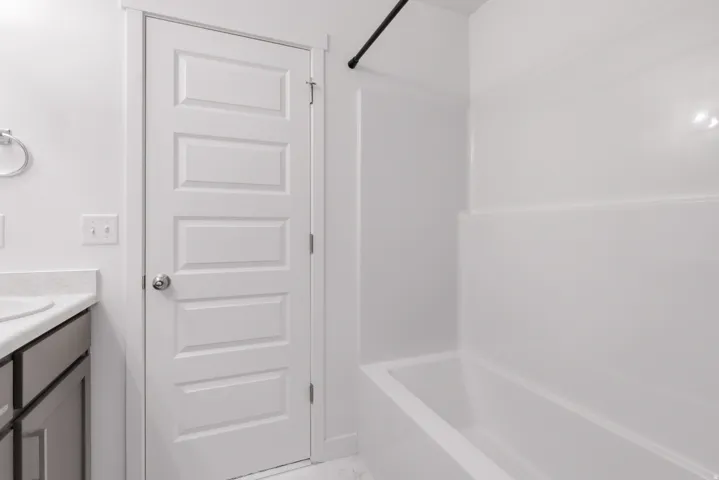 White paneled door, gray vanity cabinetry, light countertop, integral sink, and white shower/tub combination
