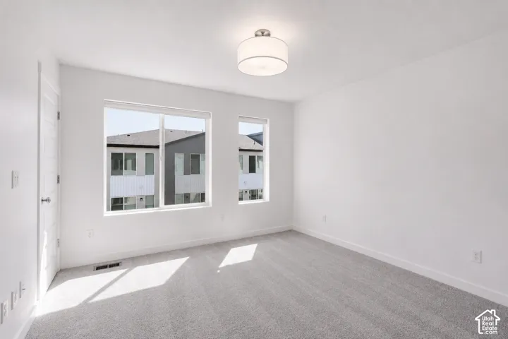 Two large windows, flush-mounted ceiling light fixture, neutral wall paint, and gray carpet flooring