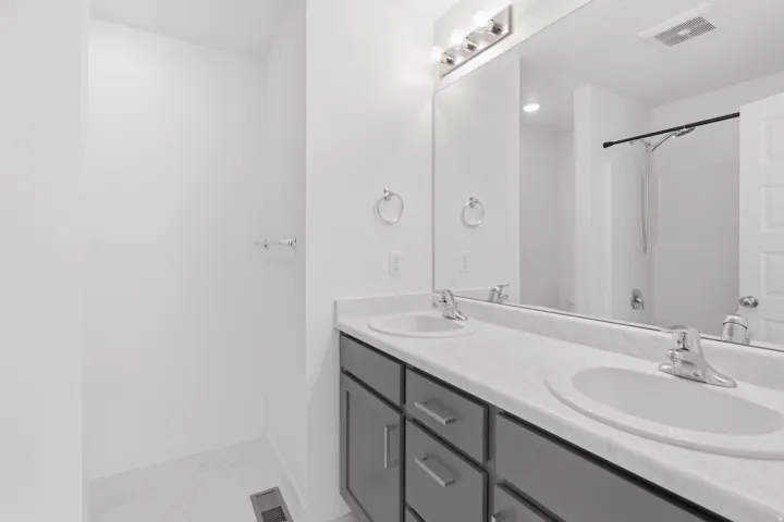 Dual vanity with undermount sinks, chrome fixtures, a large wall mirror, and a shower with a black shower rod