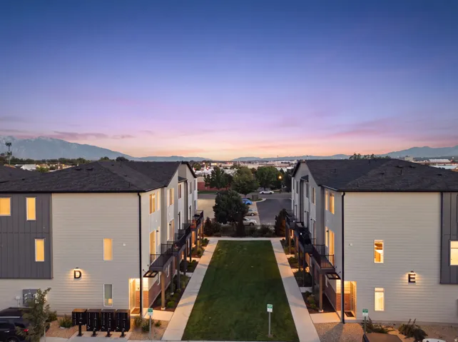 Contemporary townhomes featuring a central lawn, dark shingle roofing, and mountain backdrop
