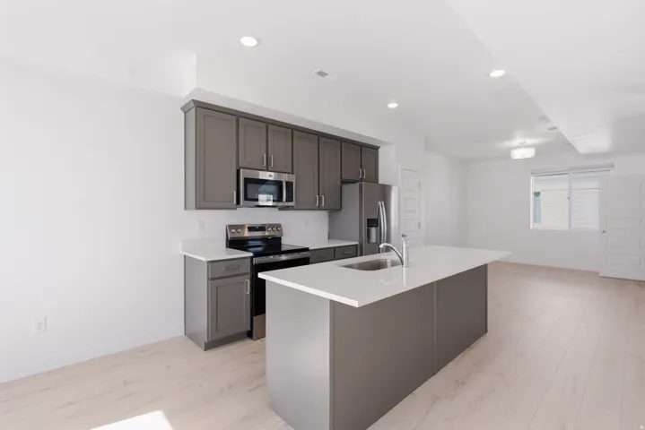 Kitchen featuring a large island with an undermount sink, stainless steel appliances, gray cabinetry, white countertops, and wood-finish flooring