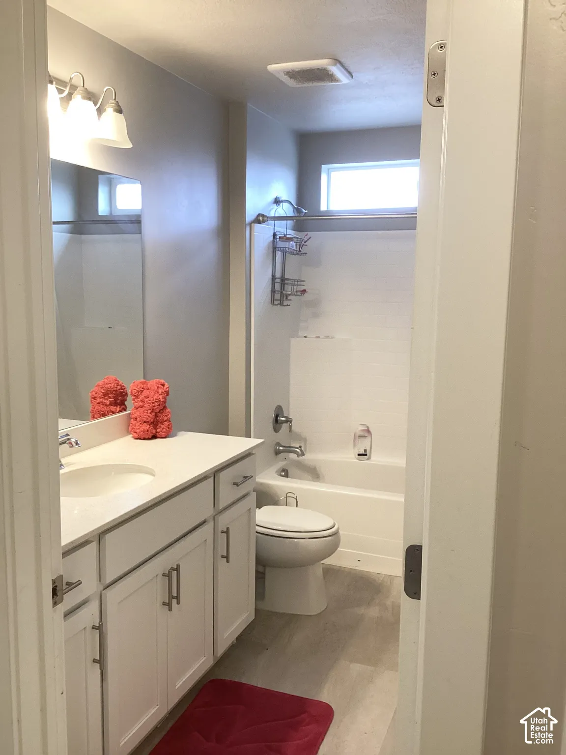 Bathroom featuring a single vanity with white cabinetry, a built-in bathtub with shower, and wood-finish flooring