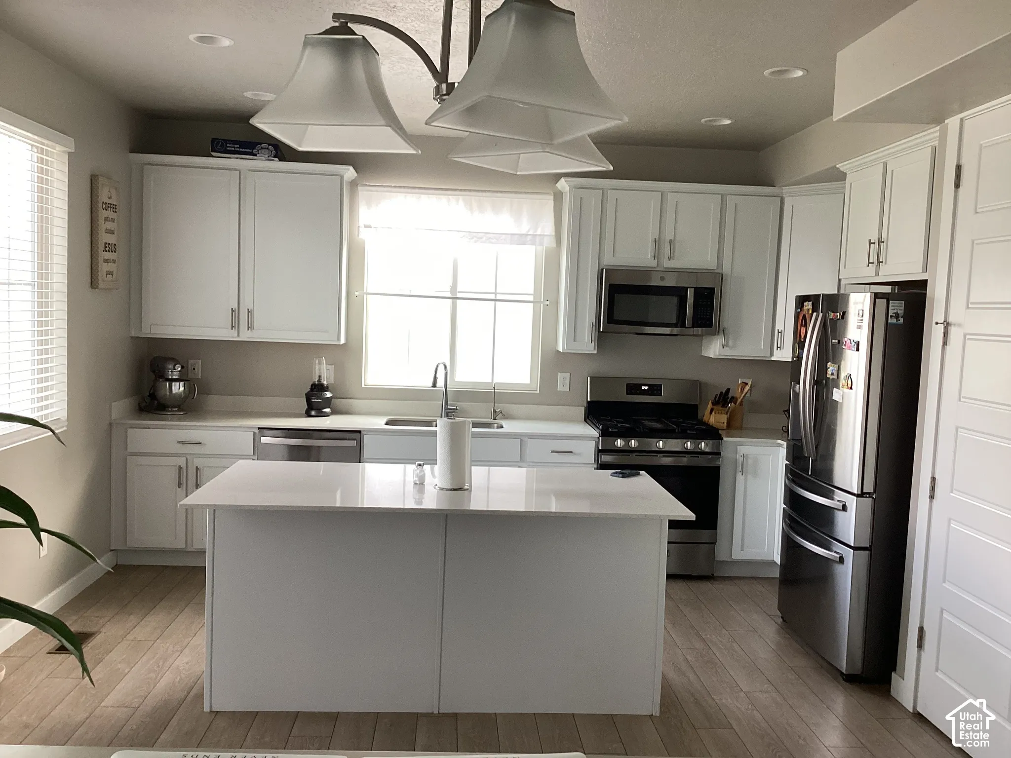 Kitchen featuring white shaker-style cabinetry, a central island with a solid surface countertop, stainless steel appliances, and wood-finish flooring