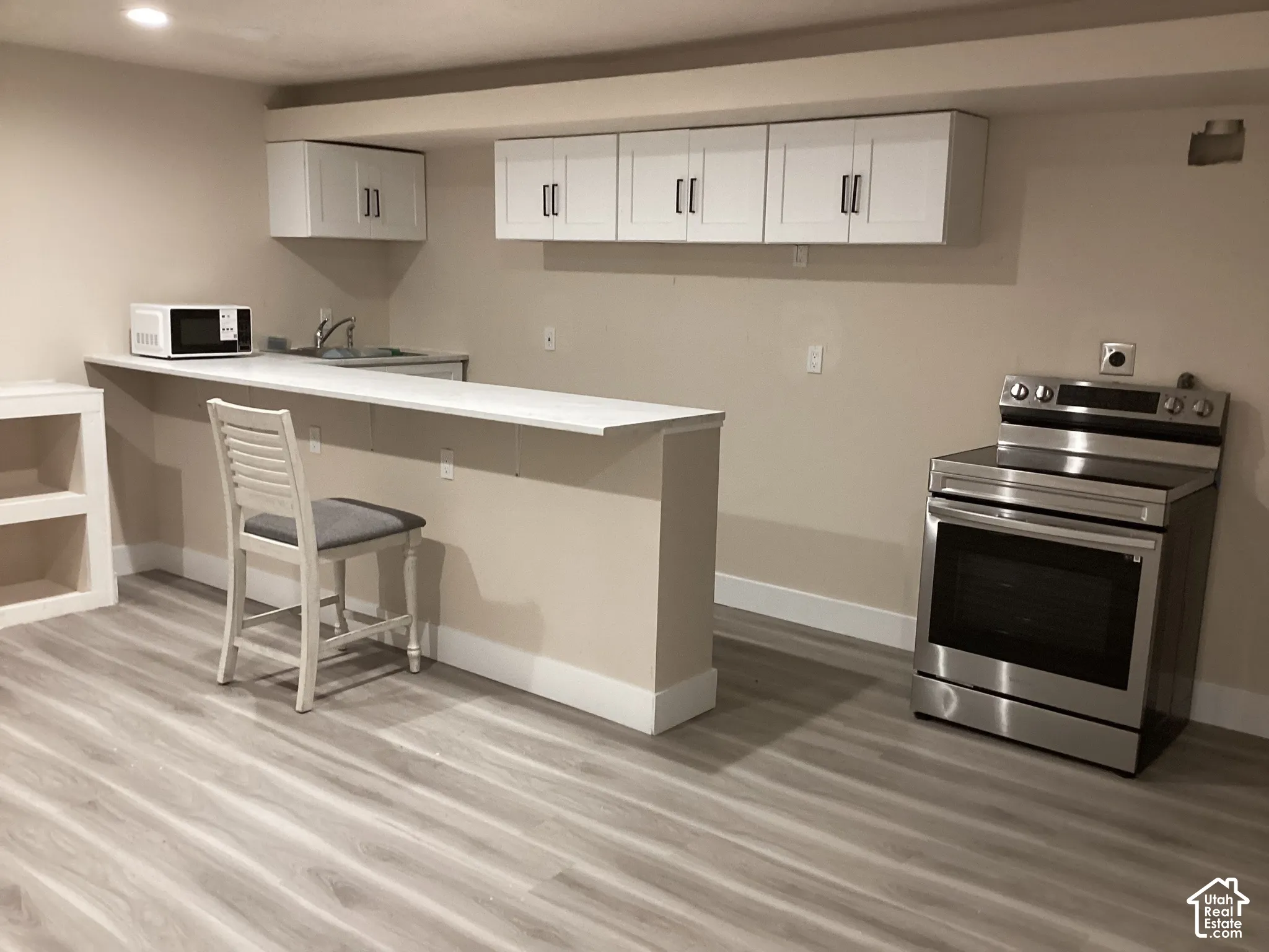 Compact kitchen area featuring wood-finish flooring, white cabinetry, a stainless steel range, and a breakfast bar