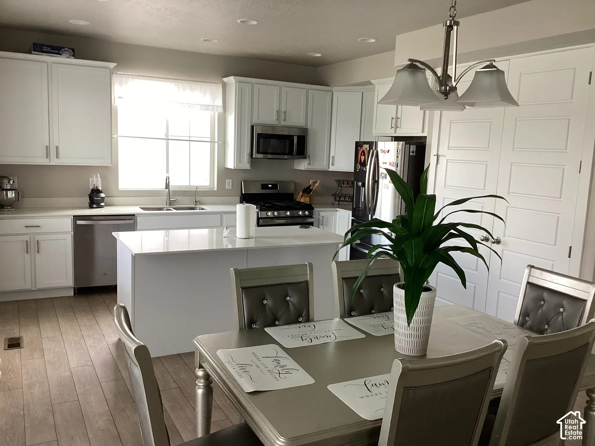 White shaker cabinetry, stainless steel appliances, central island, light wood-finish flooring, and recessed lighting