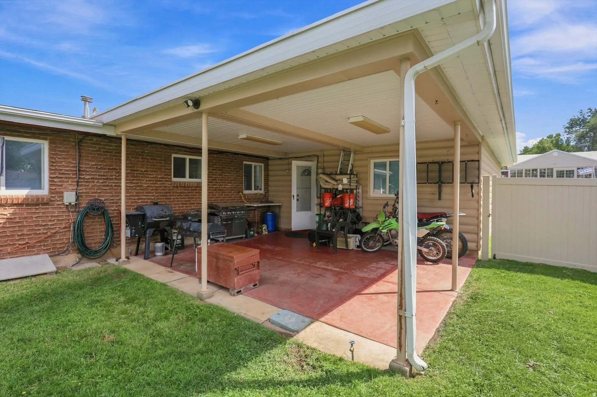 Covered patio with a concrete surface, brick exterior, and a white privacy fence