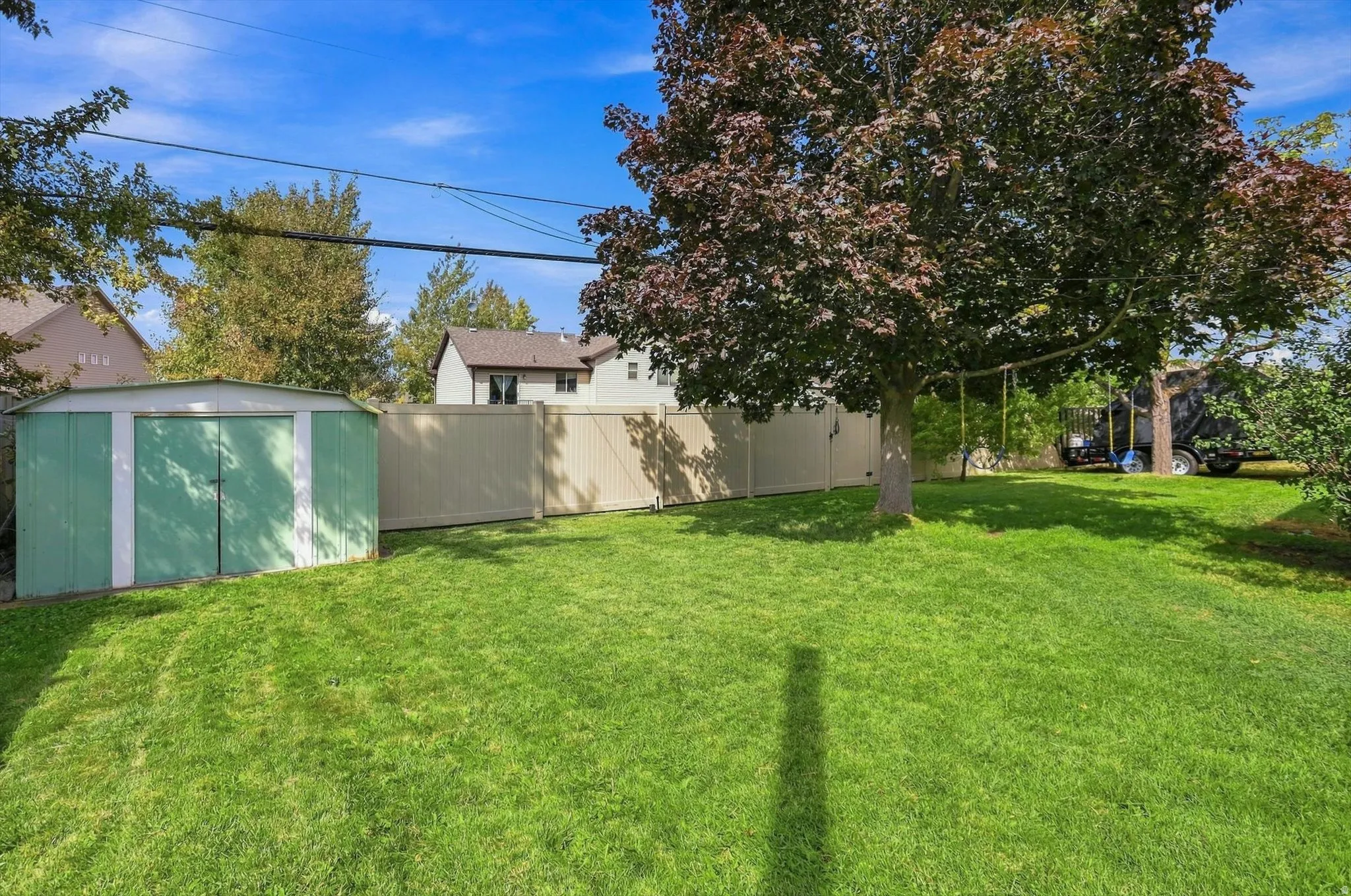 Expansive green lawn, mature tree, and a light-colored privacy fence