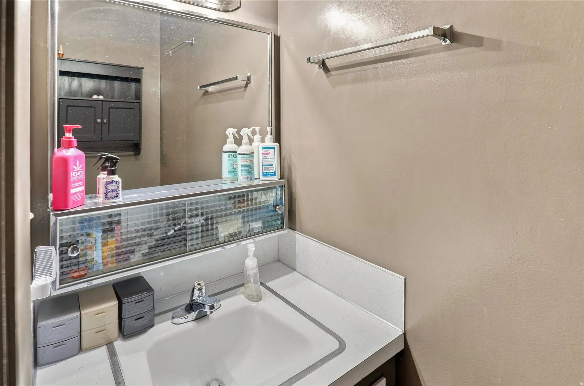 Integrated vanity with a single basin sink, wall-mounted mirror, and overhead lighting in master bathroom