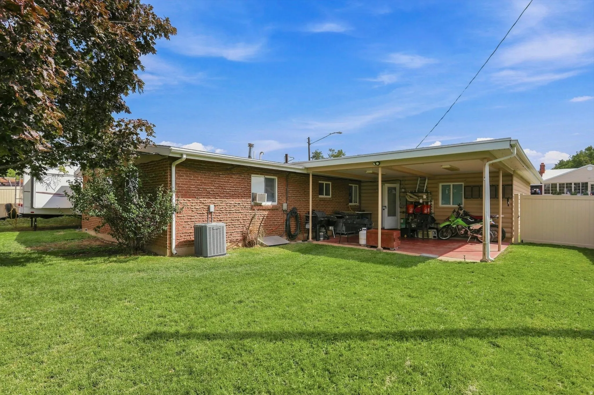 Expansive backyard featuring a manicured lawn, brick exterior, and a covered patio with a concrete surface