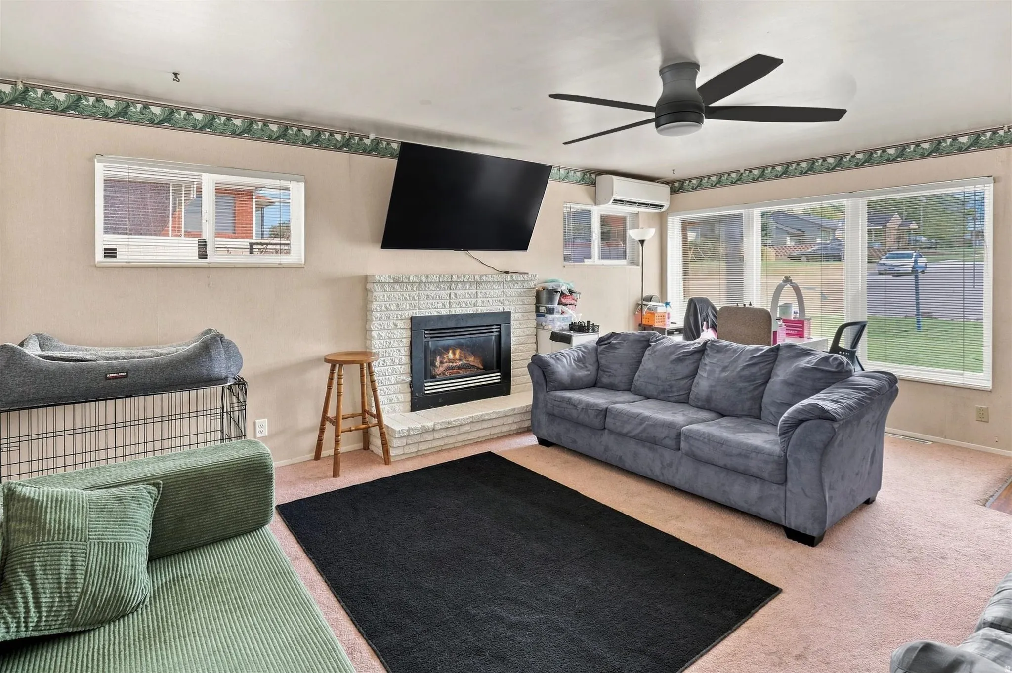 Living area featuring a brick-surround fireplace, large windows and ceiling fan