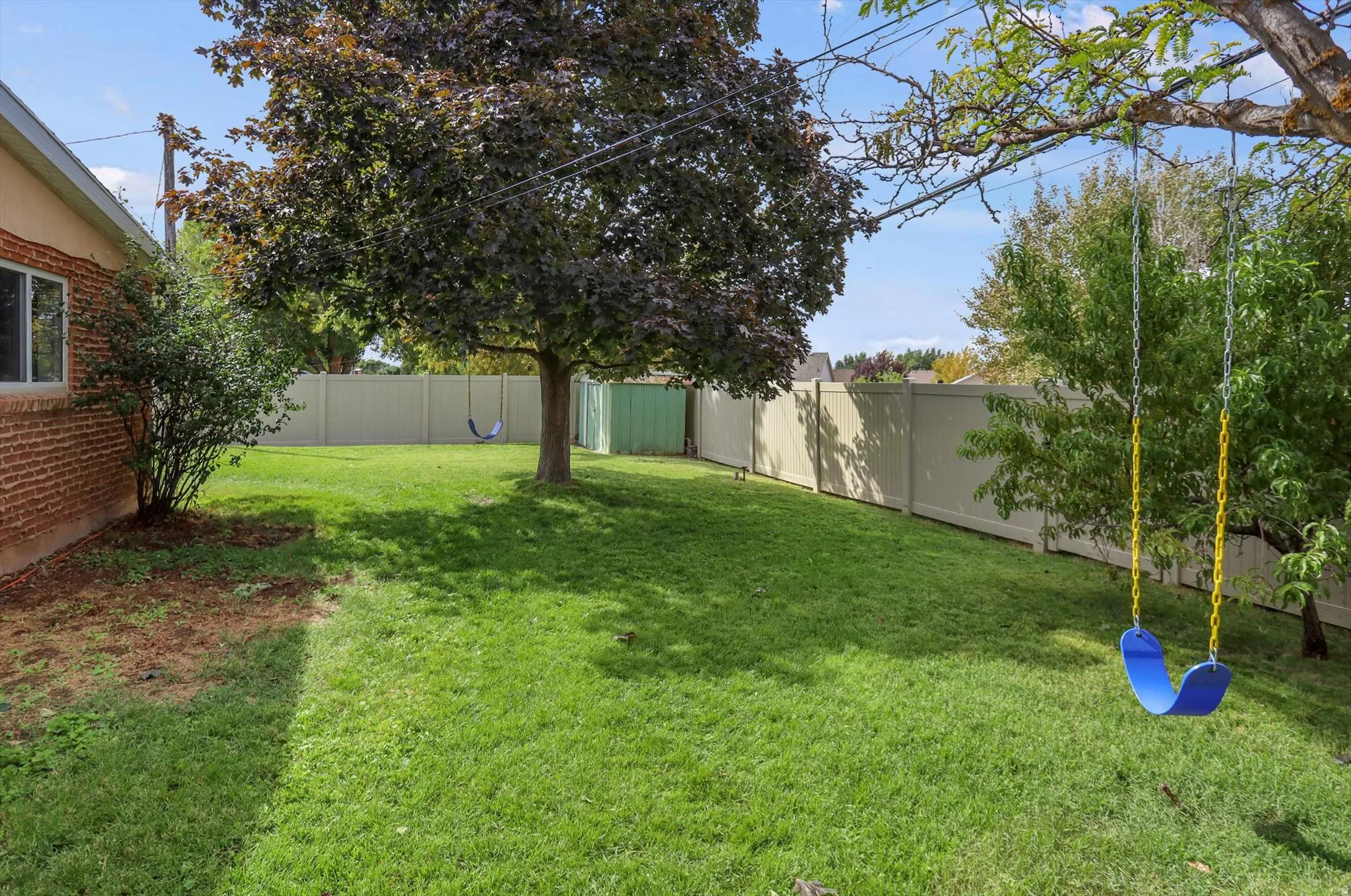 Expansive lawn area with mature trees, brick exterior, and full perimeter fencing
