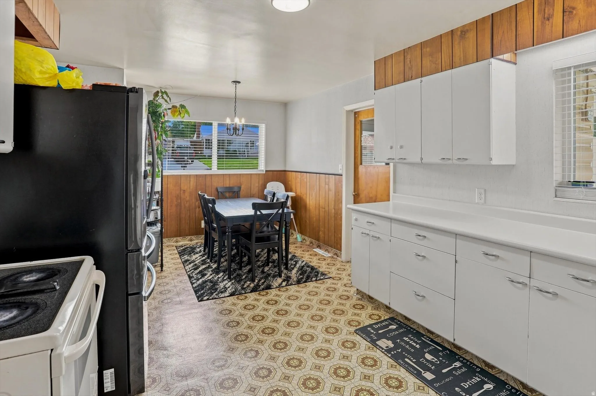 White cabinetry with silver-tone hardware, wood-panel accent wall, white countertop, window with blinds, looking into dining area