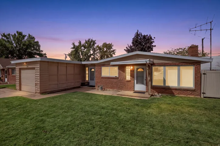 Brick exterior with a prominent chimney, attached garage, manicured lawn, and privacy fencing