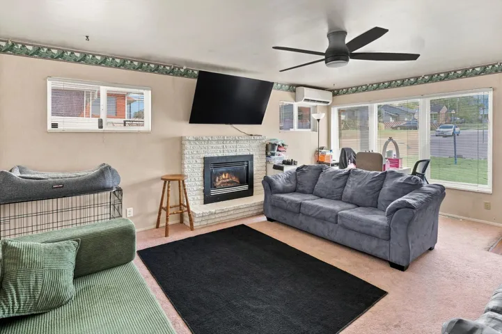 Living area featuring a brick-surround fireplace, large windows and ceiling fan