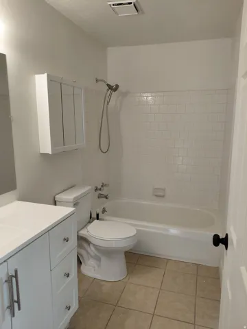 White subway tile shower surround, integrated bathtub, white vanity with shaker-style cabinetry, and tiled flooring