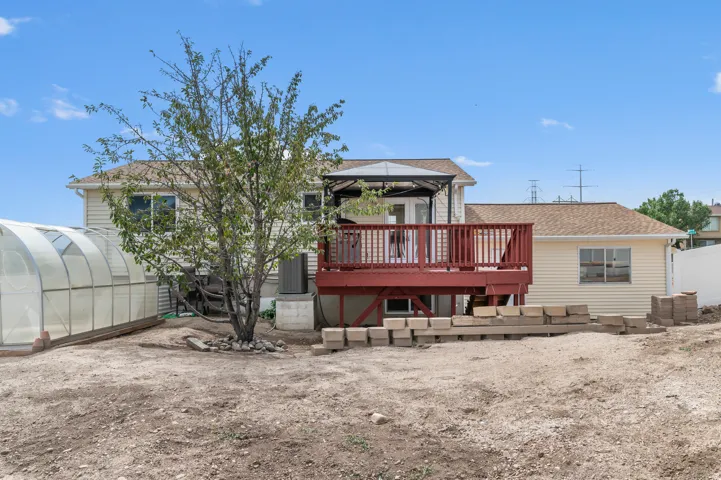 Residential property featuring a two-story main residence with covered deck and railing, single-story addition with horizontal siding, mature landscaping, and dedicated greenhouse structure