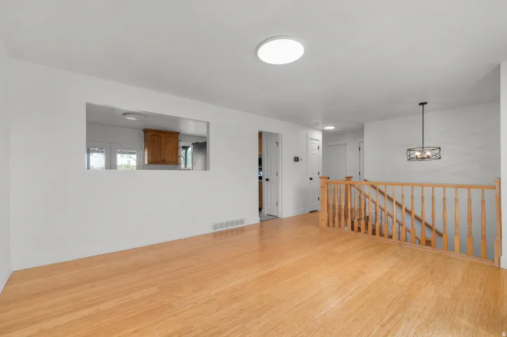 Wood-finish flooring throughout, a pass-through opening to the kitchen, and a staircase with a wood railing