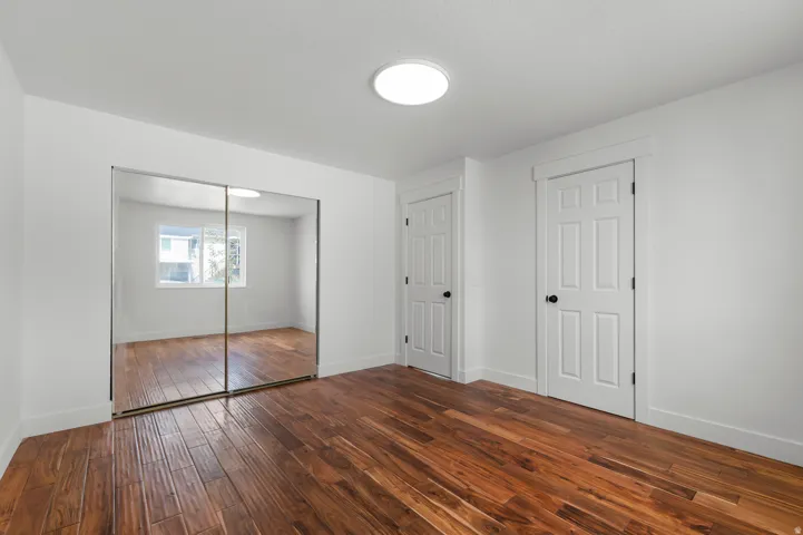 Wood-finish flooring throughout, bright white walls, mirrored sliding closet doors.