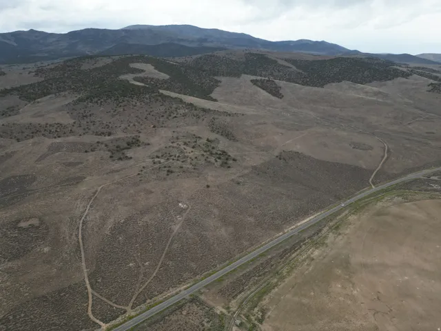 Expansive undeveloped land with a paved road frontage, natural terrain, and distant mountain ranges
