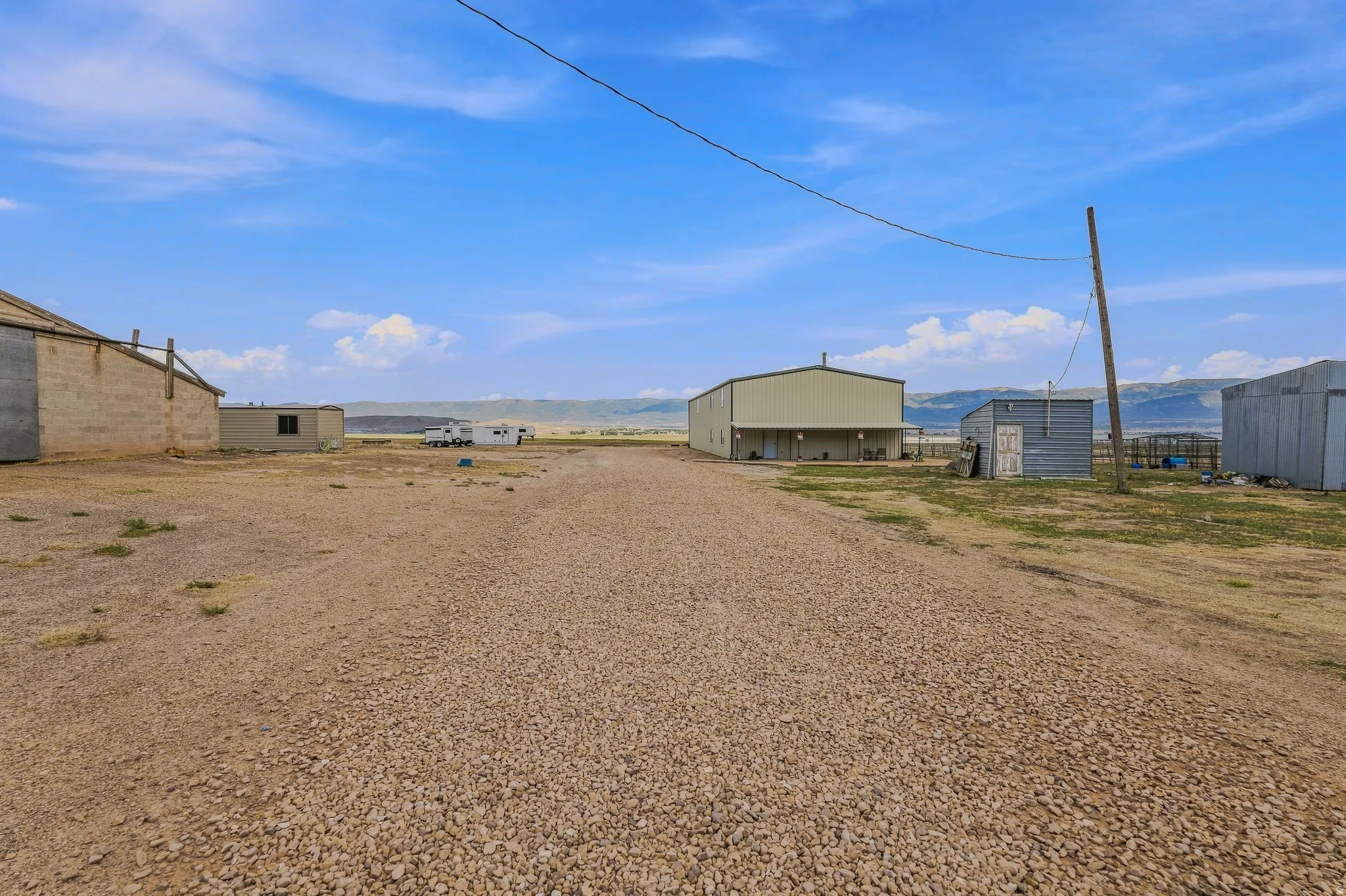 Gravel driveway leading to multiple outbuildings, including a large metal-sided structure with a covered porch