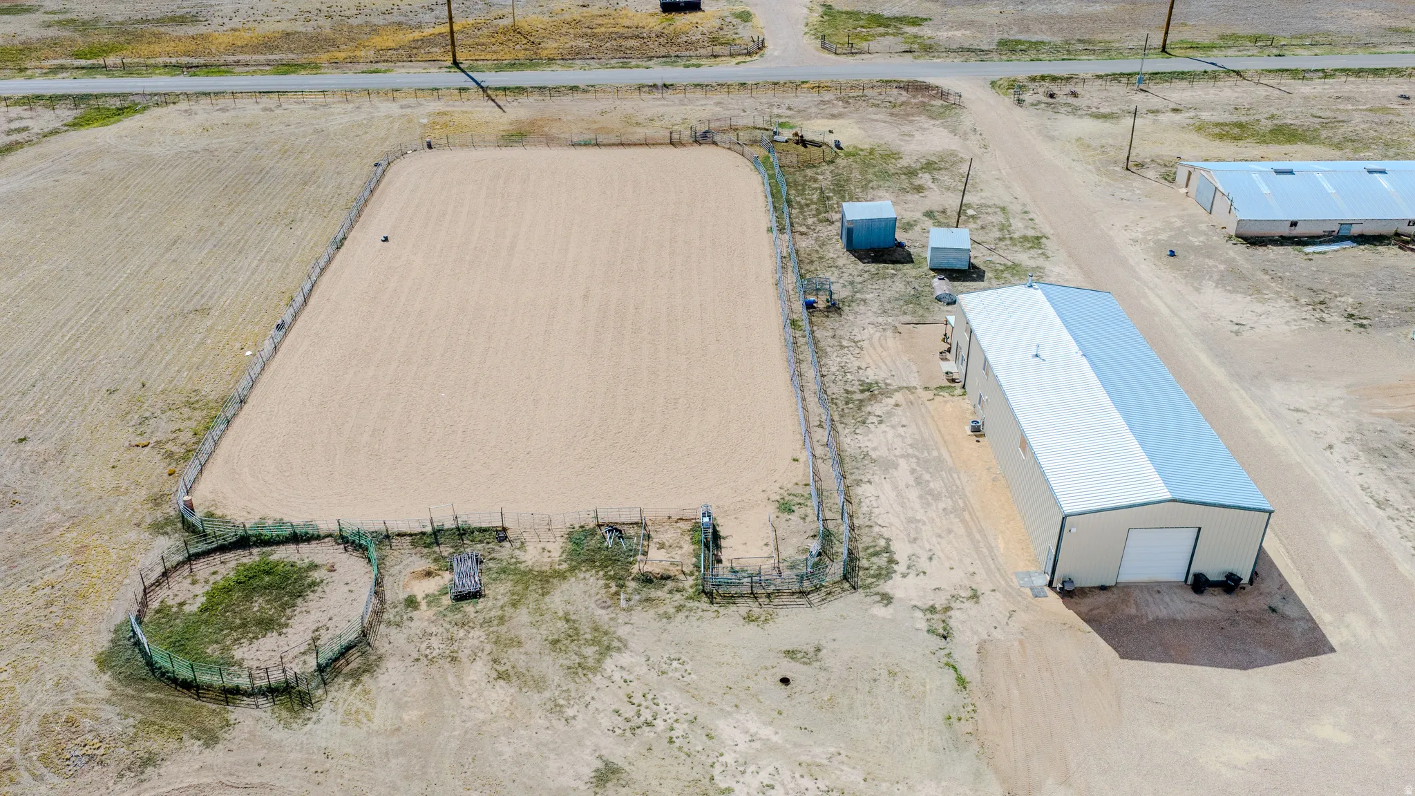 Expansive outdoor arena, round pen, large metal building with a roll-up door, and additional storage sheds