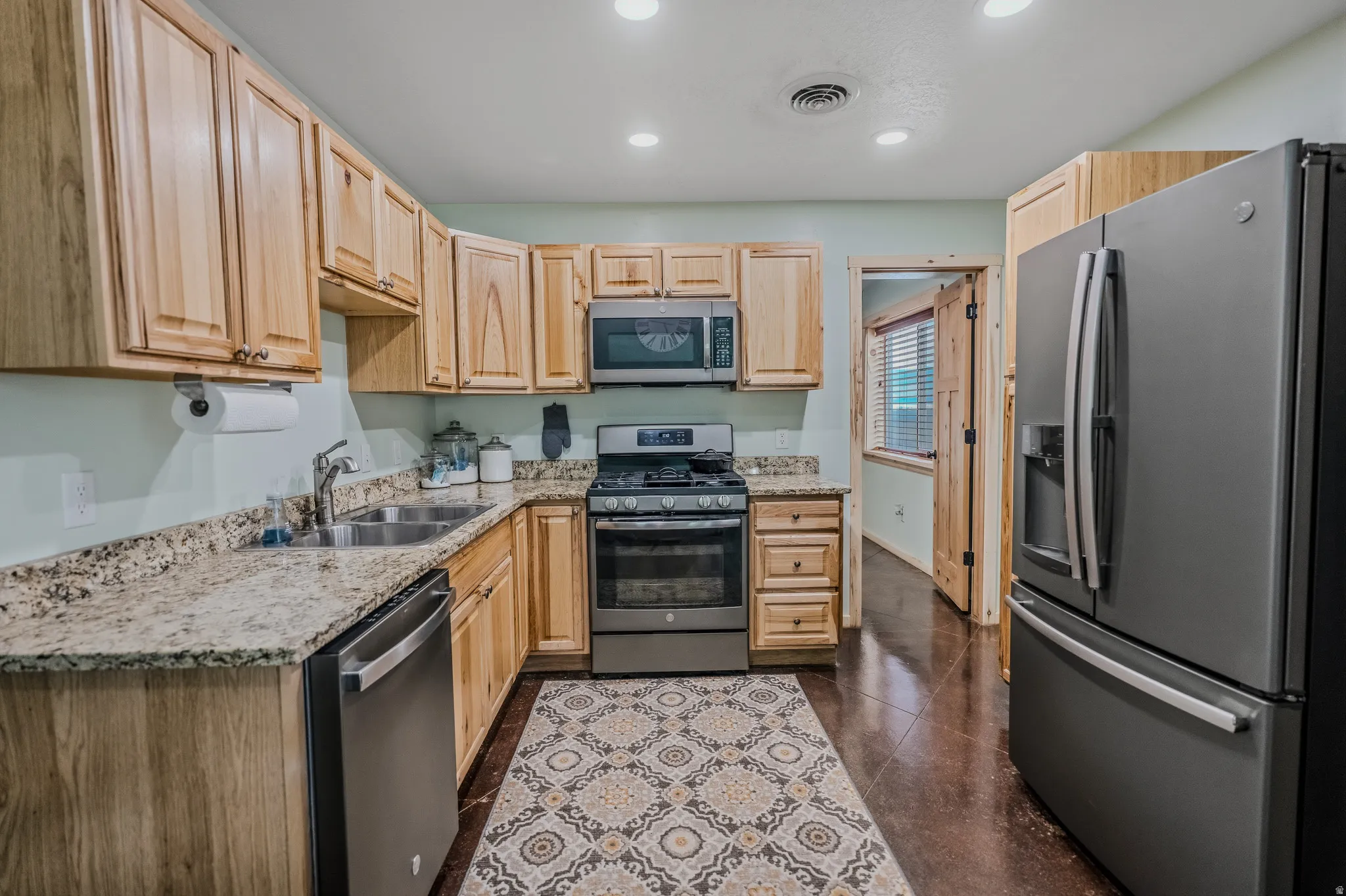 Kitchen featuring wood cabinetry, stainless steel appliances, granite-style countertops, and recessed lighting