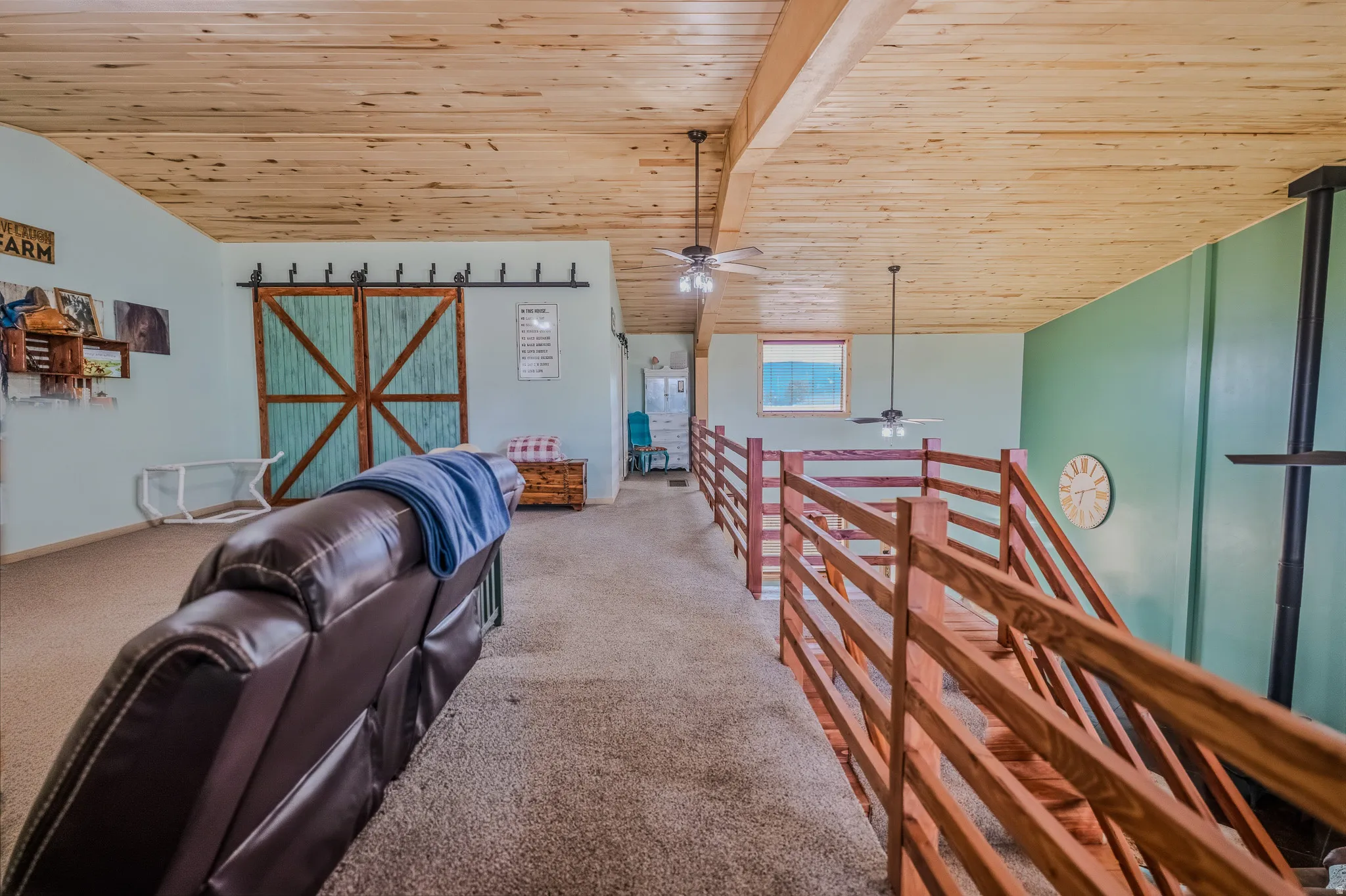 Wood-paneled ceiling, exposed beam, wood-finish railings, ceiling fan lighting, and a barn door