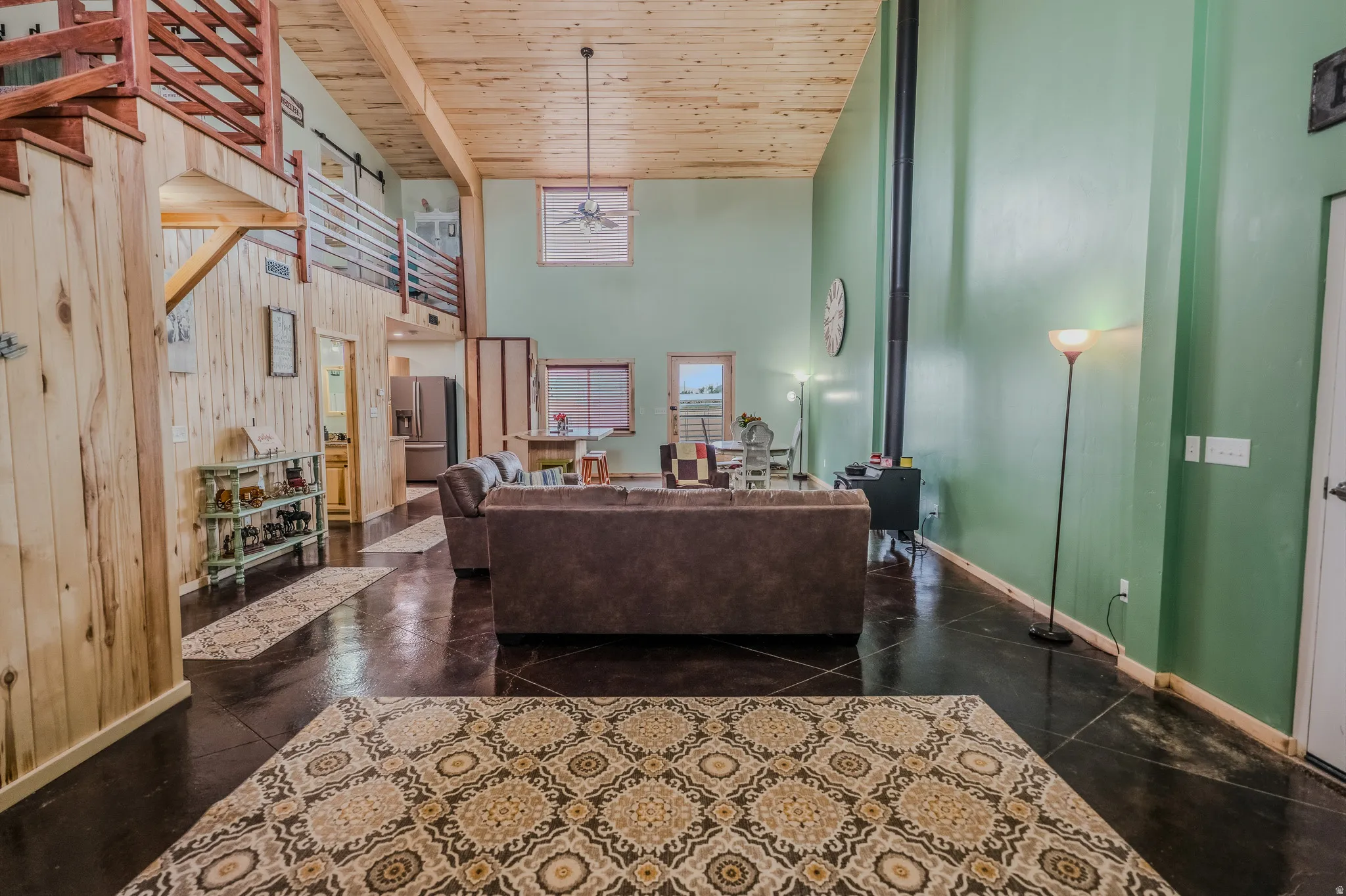 High ceilings with wood-finish planks, dark flooring, and a visible wood-burning stove with a tall flue