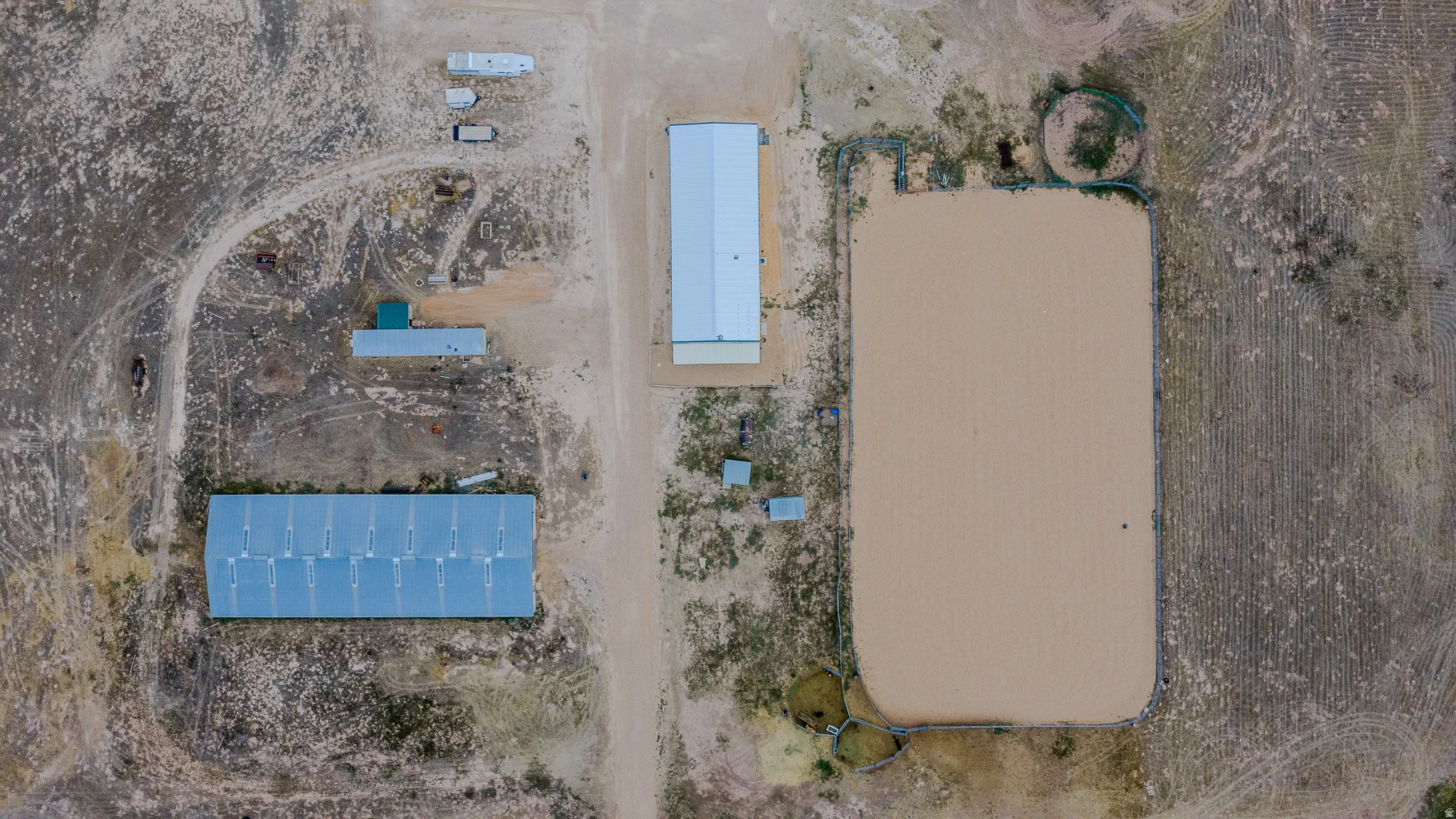 Expansive land featuring multiple structures, a large sand arena, and a smaller circular pen