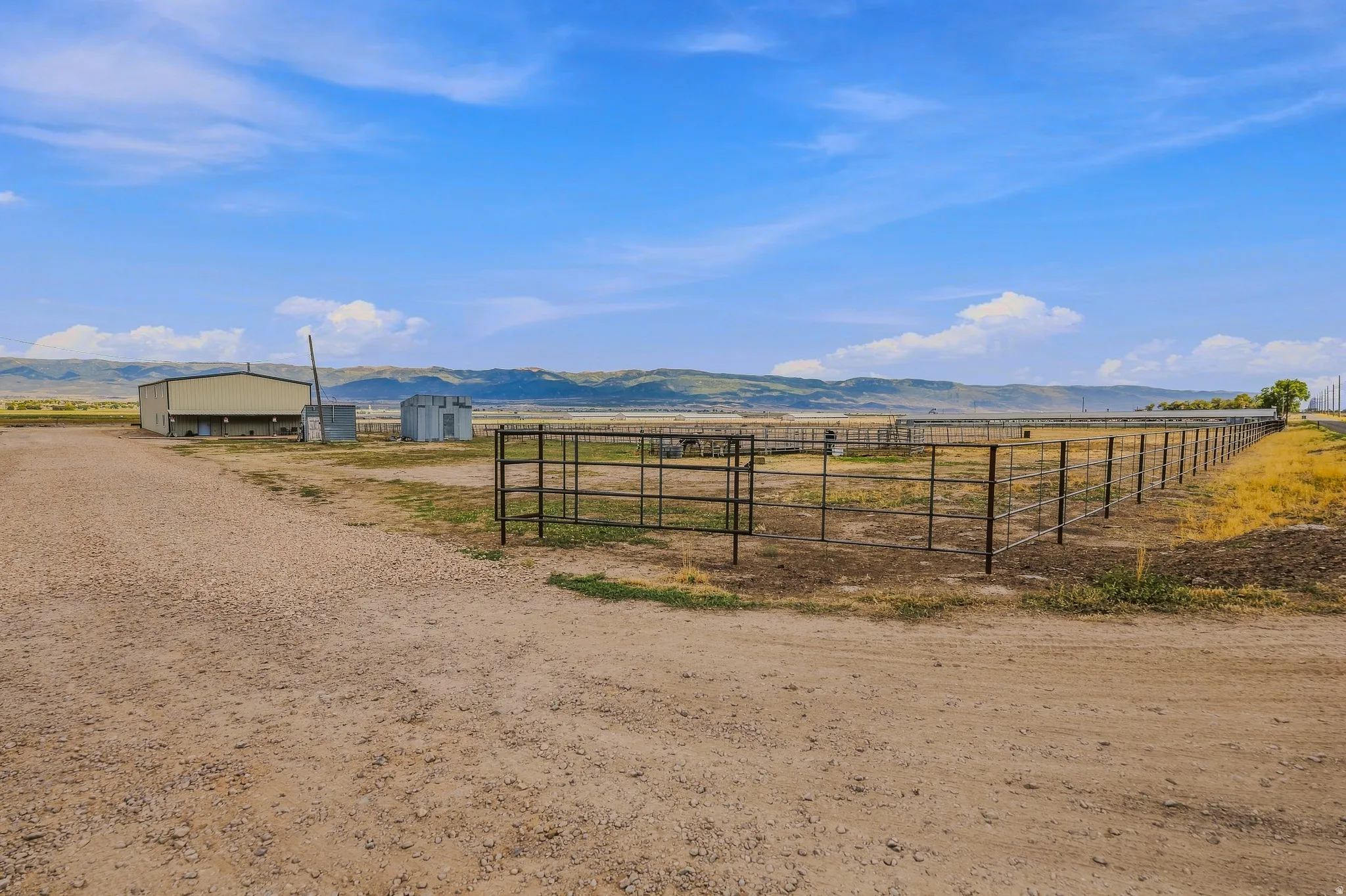 Gravel drive leading to a large metal-sided outbuilding with multiple pens, extensive fencing, and distant mountain topography