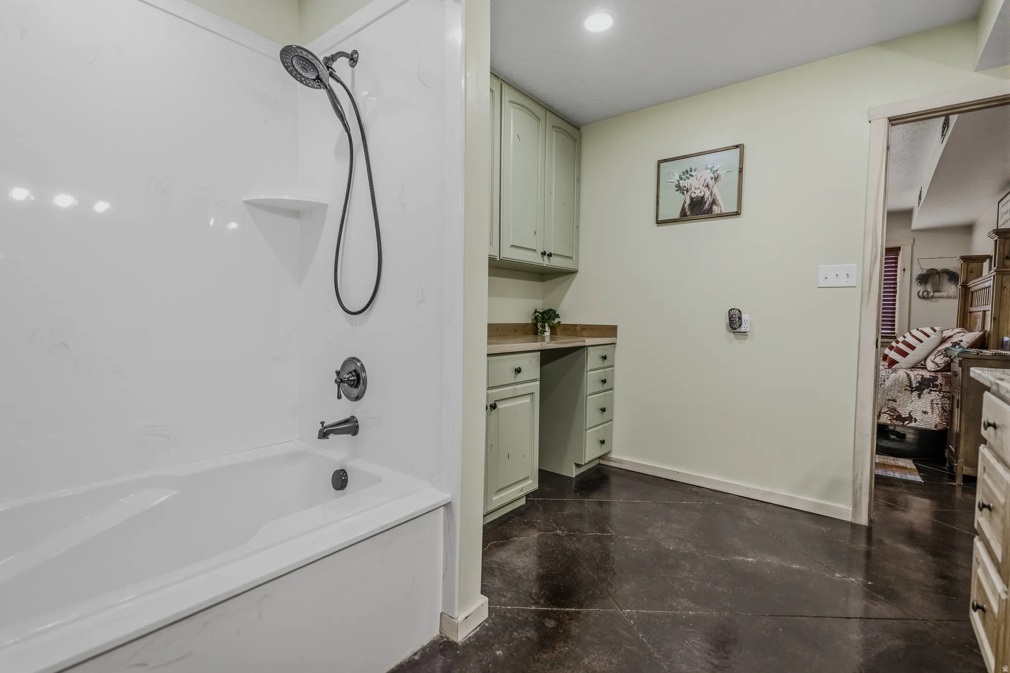 Bathtub with a black shower fixture, built-in cabinetry with a light-toned countertop, and dark-toned flooring