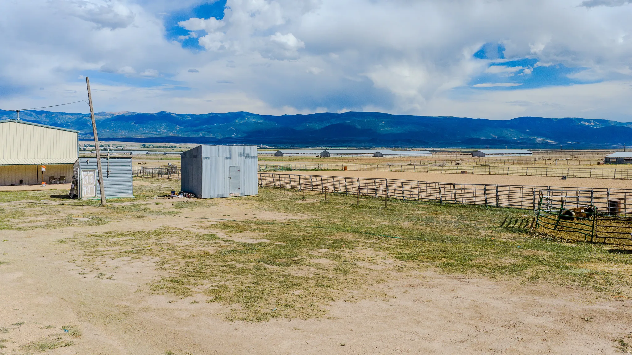 Expansive open terrain featuring mountain range backdrop, fenced corrals, and a large metal-sided outbuilding