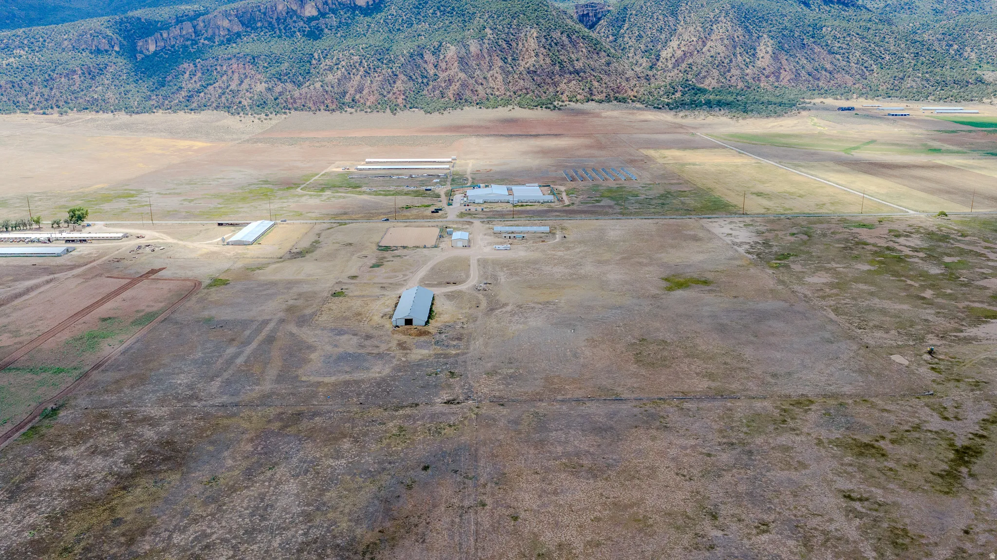 Expansive rural property featuring multiple outbuildings, open fields, and distant mountainous terrain