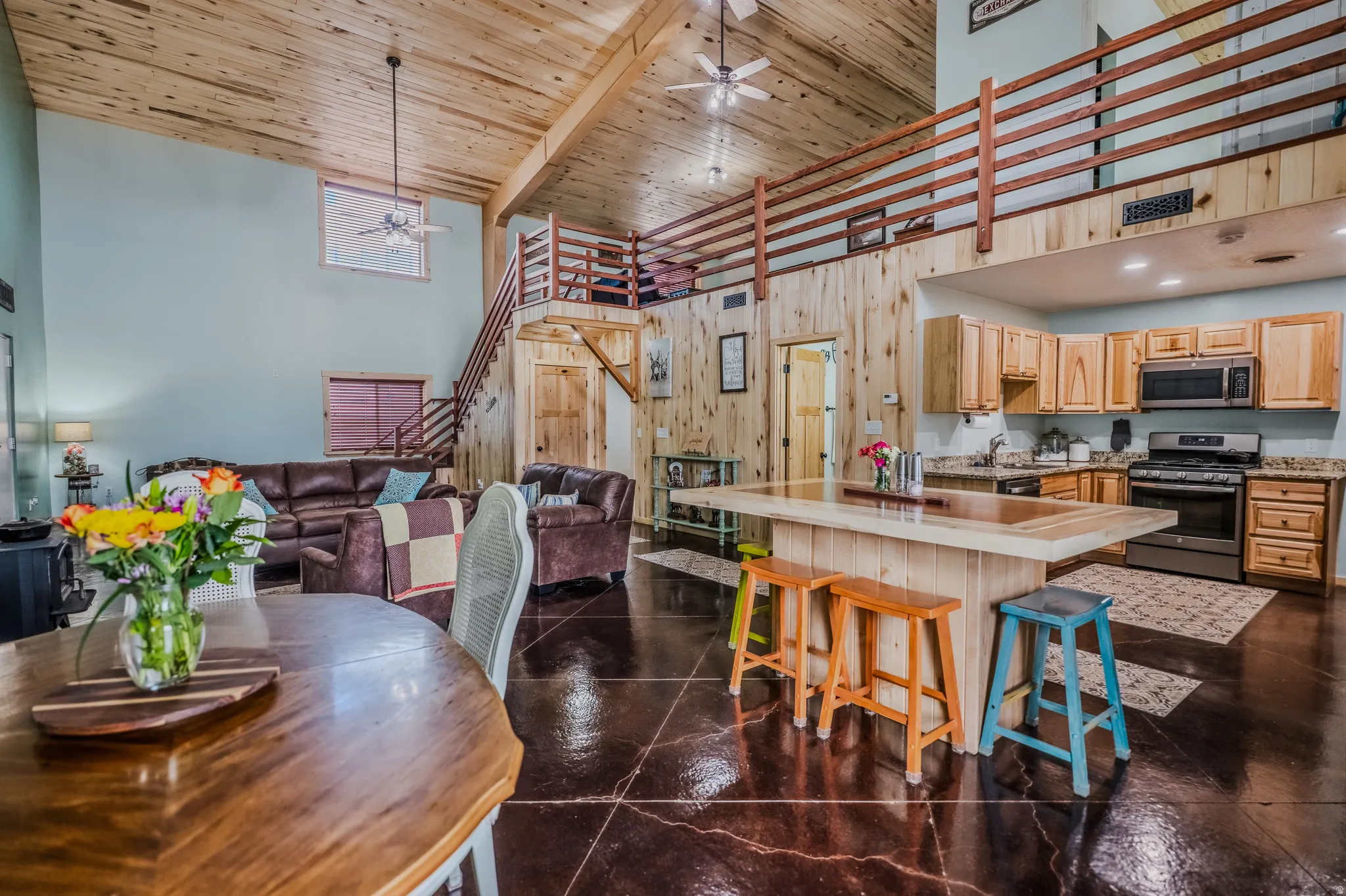 Vaulted wood-finish ceilings, wood-finish accent walls, wood-finish flooring, wood-finish kitchen cabinetry, and stainless steel appliances