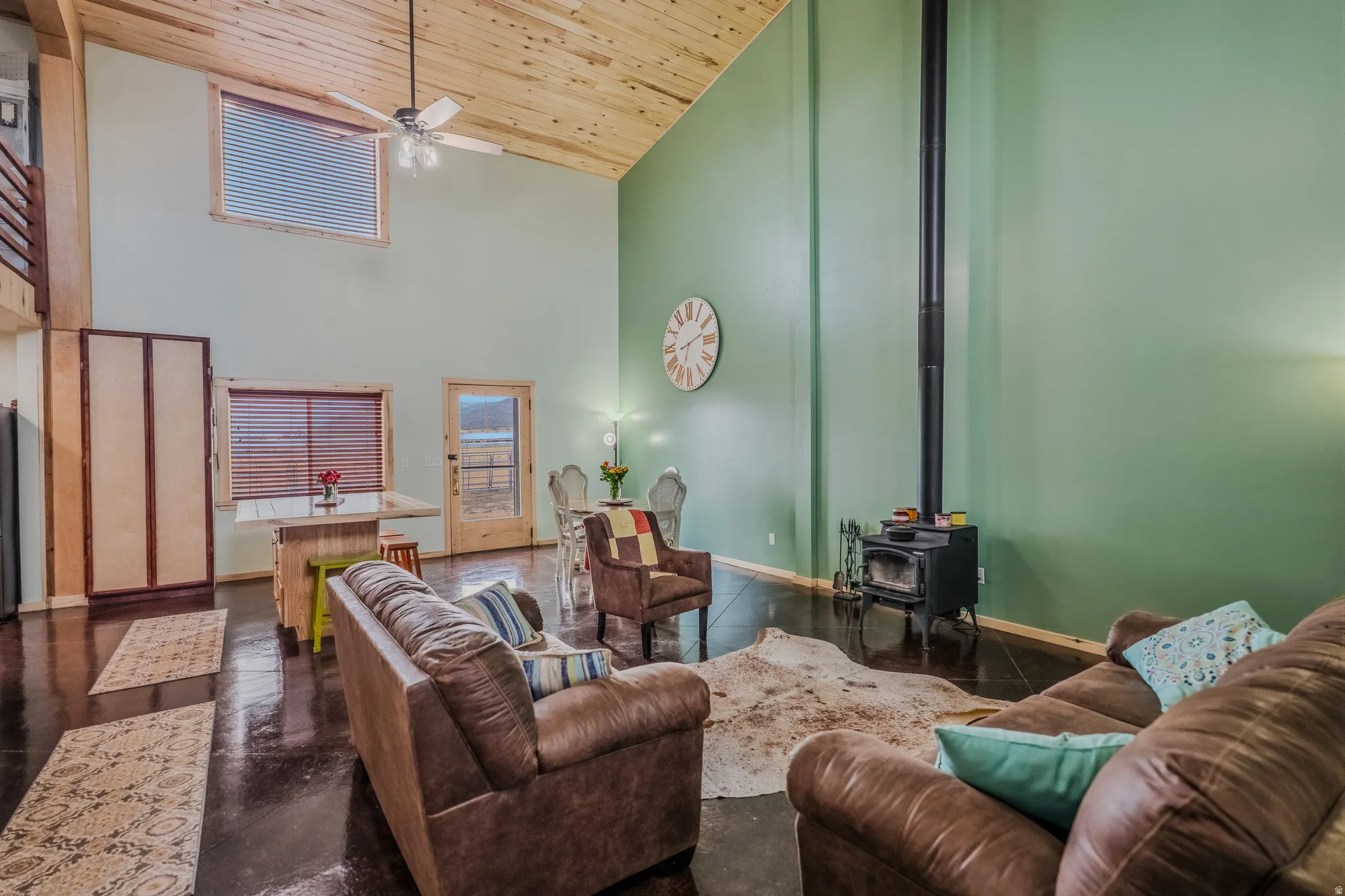 Vaulted wood-paneled ceiling with exposed beams, wood-finish flooring, wood-burning stove, and a ceiling fan with integrated lighting