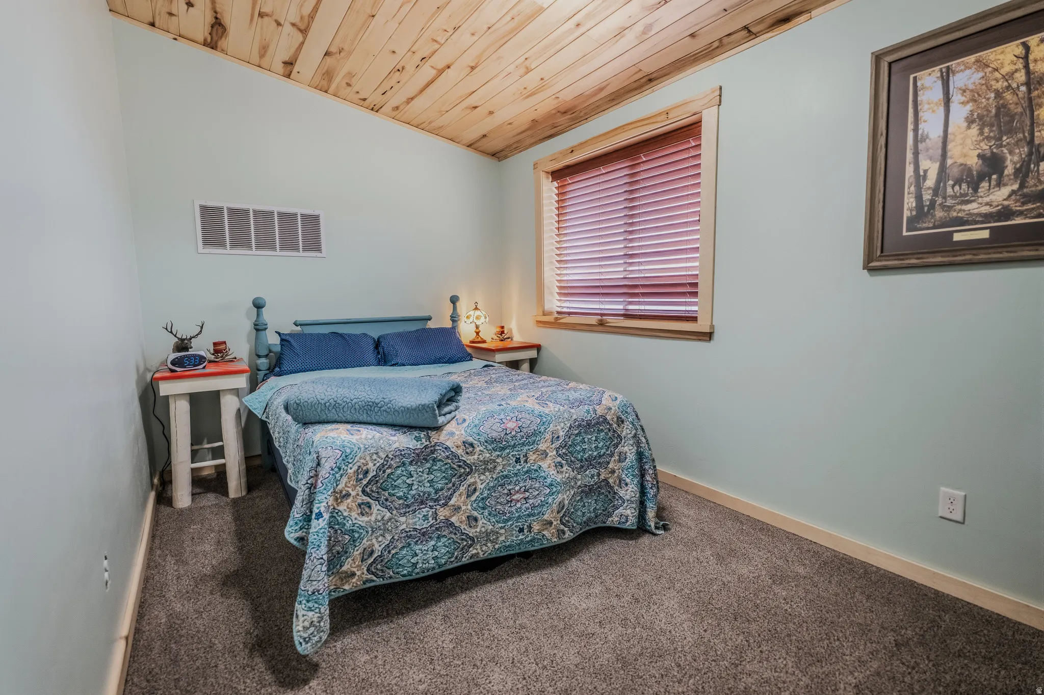 Vaulted wood-paneled ceiling, light blue walls, wood-trimmed window, gray carpet, and white electrical outlets