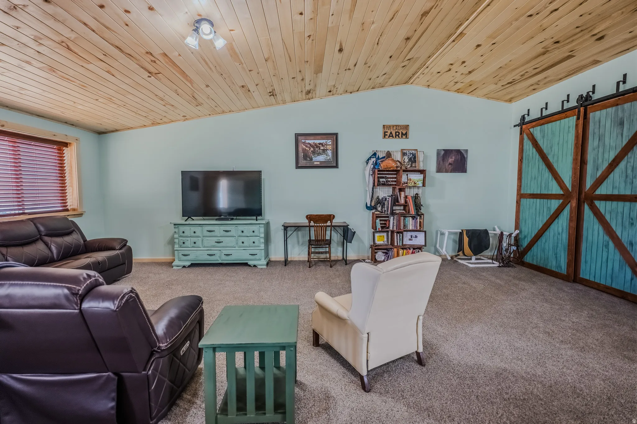 Vaulted wood-paneled ceiling, light blue wall paint, window with wood trim and blinds, and dual sliding barn doors