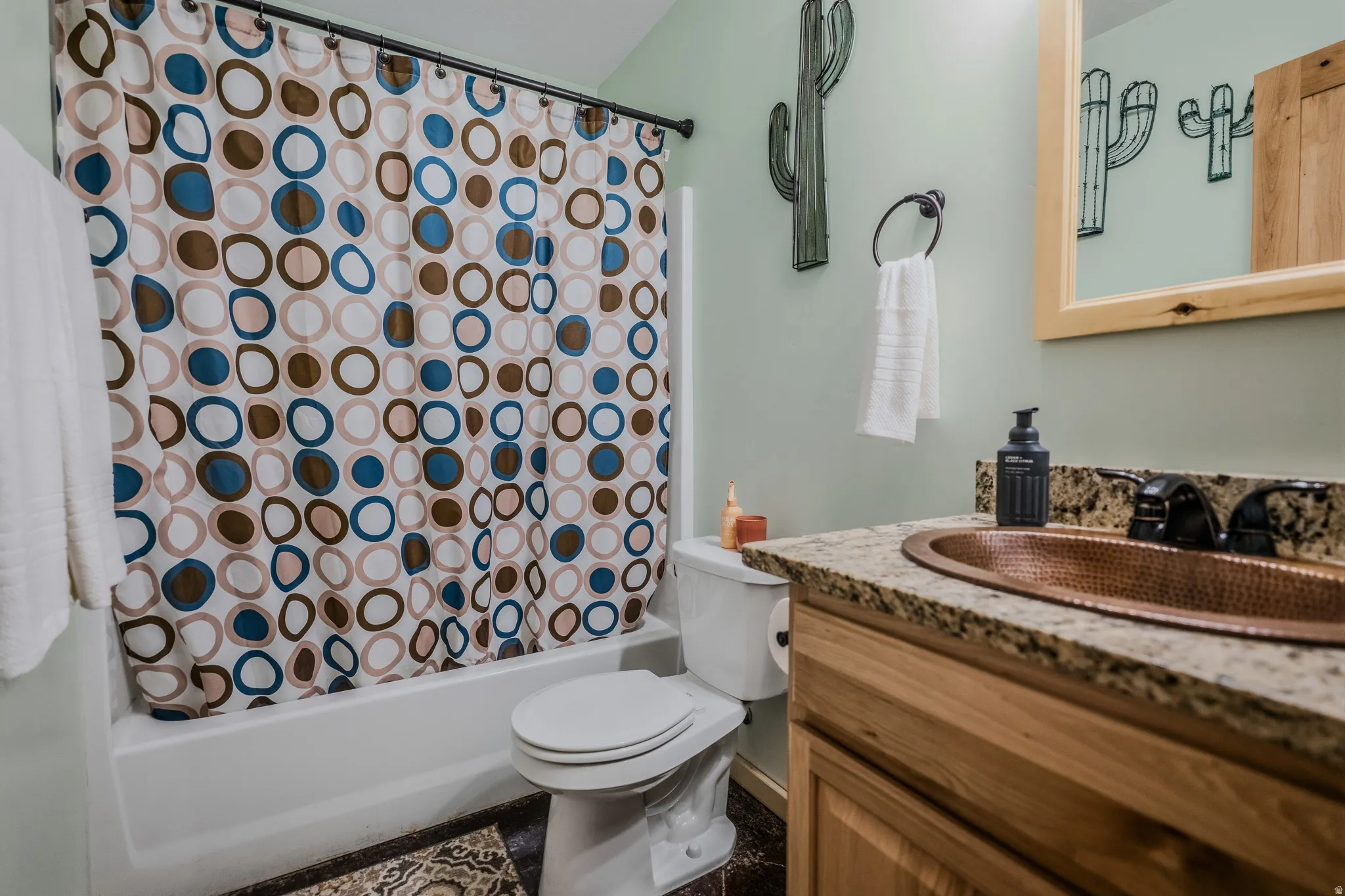 White bathtub with shower, toilet, wood-finish vanity with countertop, and a copper sink