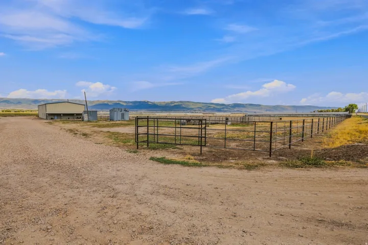 Expansive agricultural land featuring a metal-sided outbuilding, multiple fenced enclosures, and a gravel drive