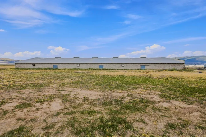 Spacious agricultural building with a metal roof, multiple access doors, and a large open field