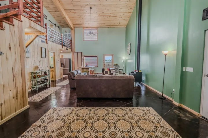 High ceilings with wood-finish planks, dark flooring, and a visible wood-burning stove with a tall flue
