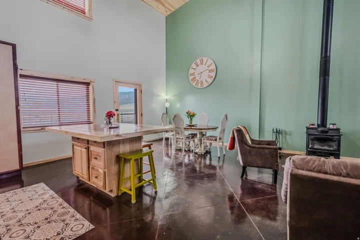 Spacious room with high ceilings, polished concrete flooring, exposed wood beams, a wood-burning stove, and a wood-framed window with blinds