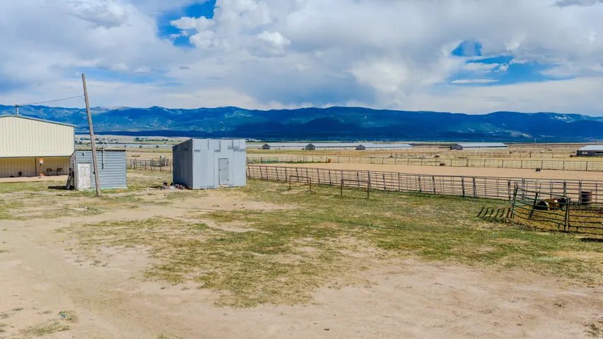 Expansive open terrain featuring mountain range backdrop, fenced corrals, and a large metal-sided outbuilding