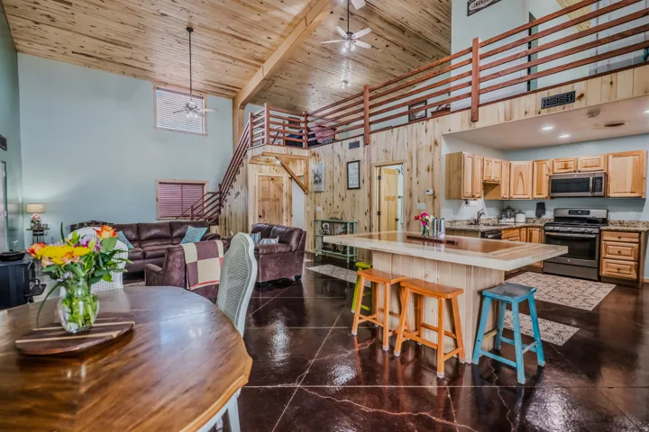 Vaulted wood-finish ceilings, wood-finish accent walls, wood-finish flooring, wood-finish kitchen cabinetry, and stainless steel appliances