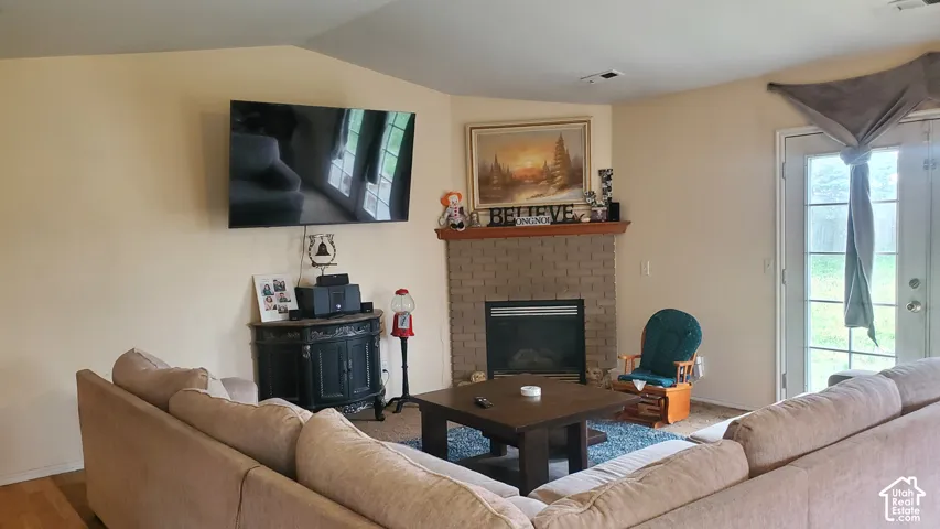 Vaulted ceiling, corner fireplace with a brick surround, wood-finish mantel, and double glass-paneled exterior door