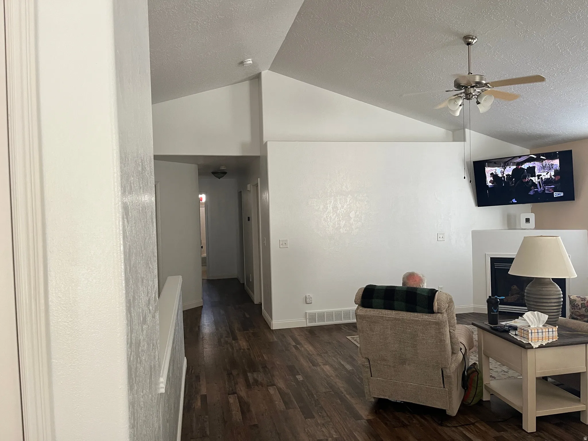 Vaulted ceilings, wood-finish flooring, ceiling fan, and a fireplace with a white mantel