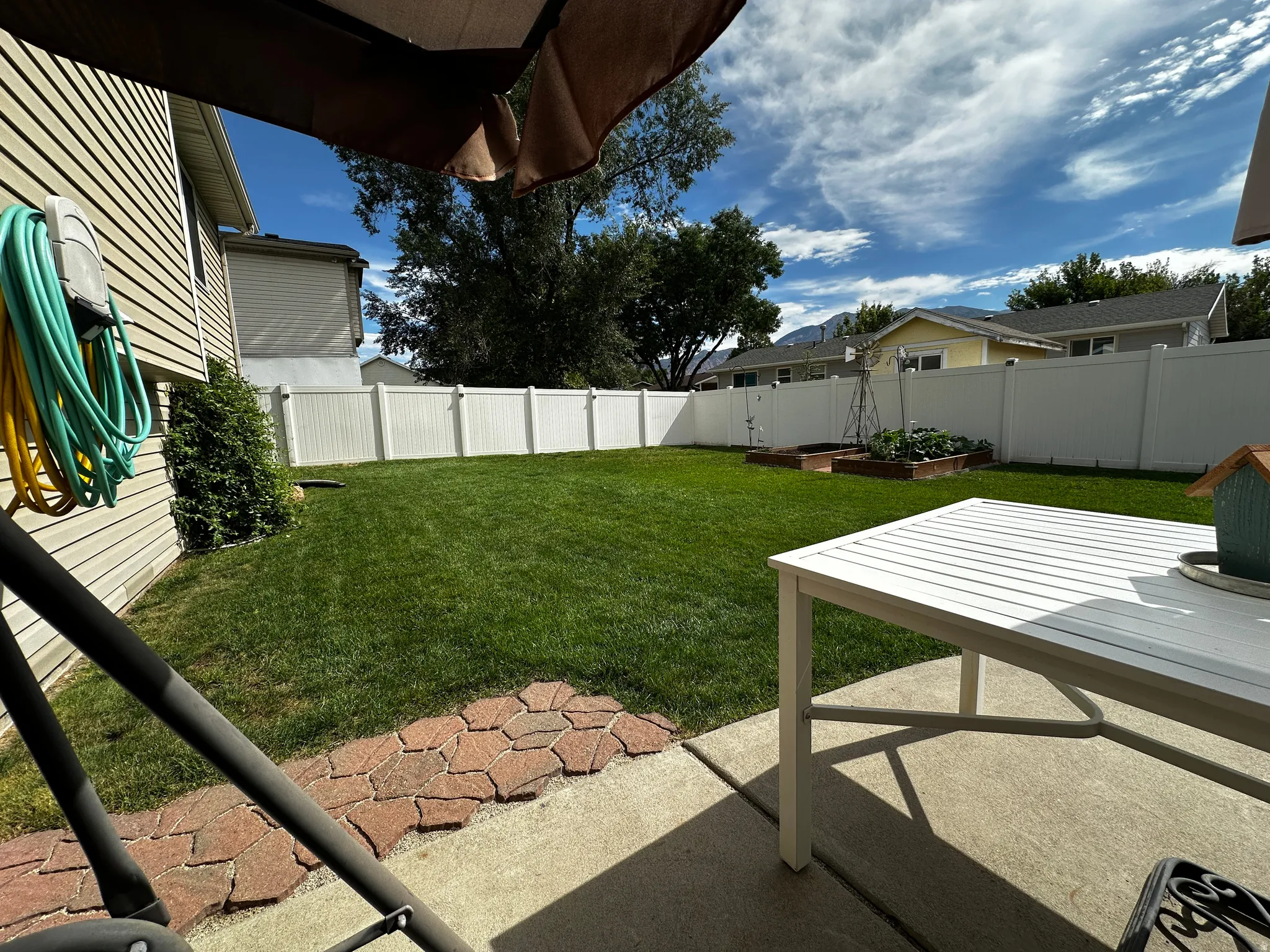 Expansive backyard featuring a green lawn, white privacy fencing, concrete patio, and garden beds