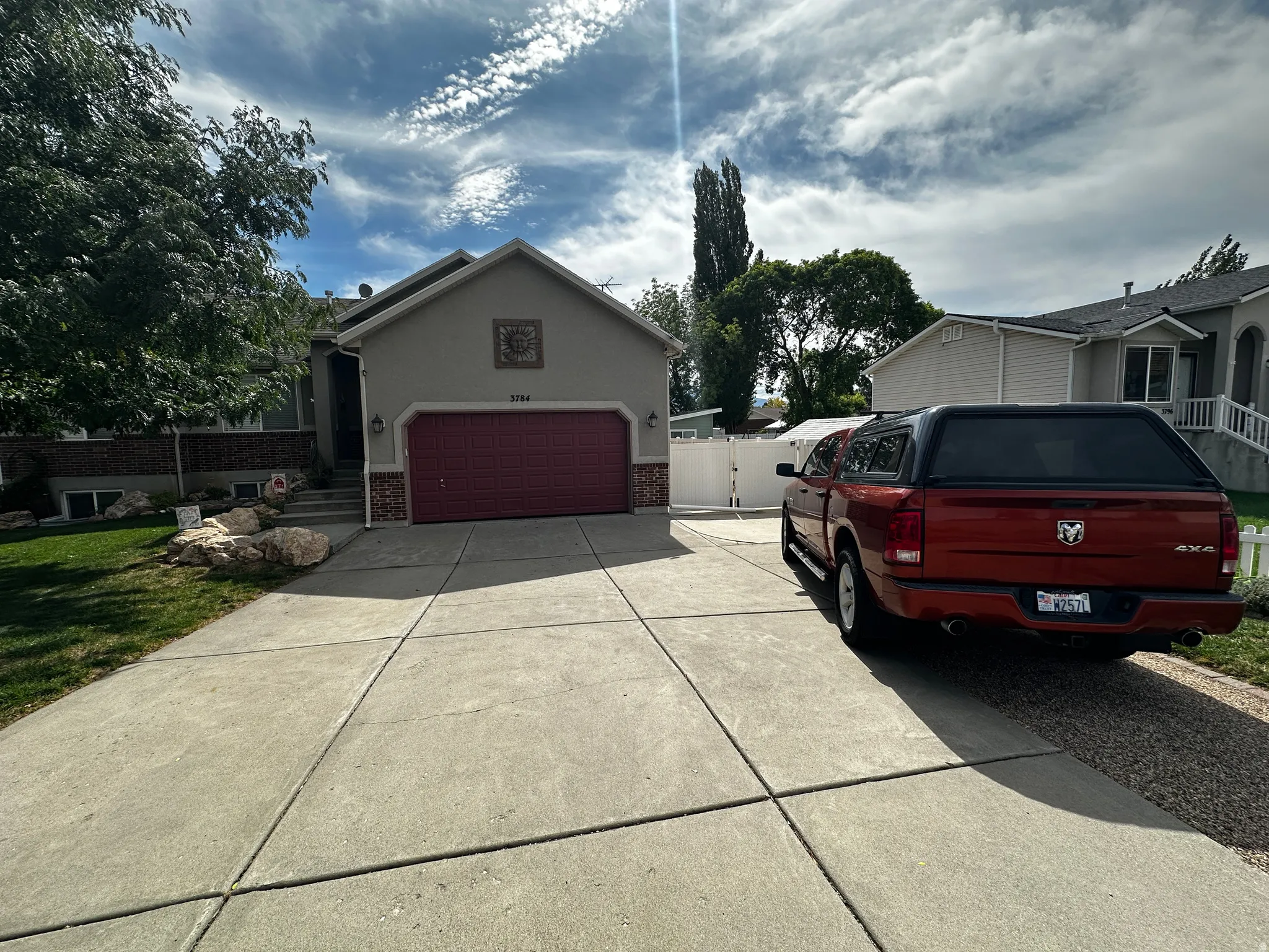 Property exterior featuring a concrete driveway, attached two-car garage with a red door, brick façade accents, and an ornamental wall detail
